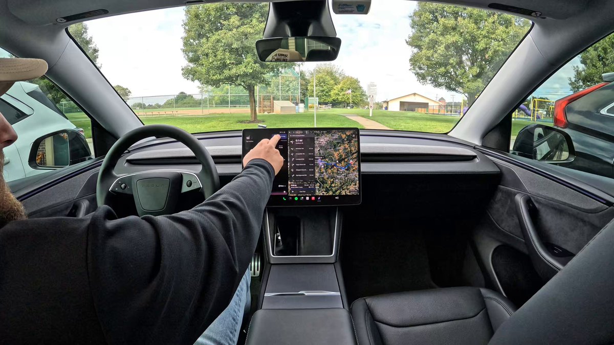 A driver points at the navigation map on a Tesla center screen while parked near a recreation area.
