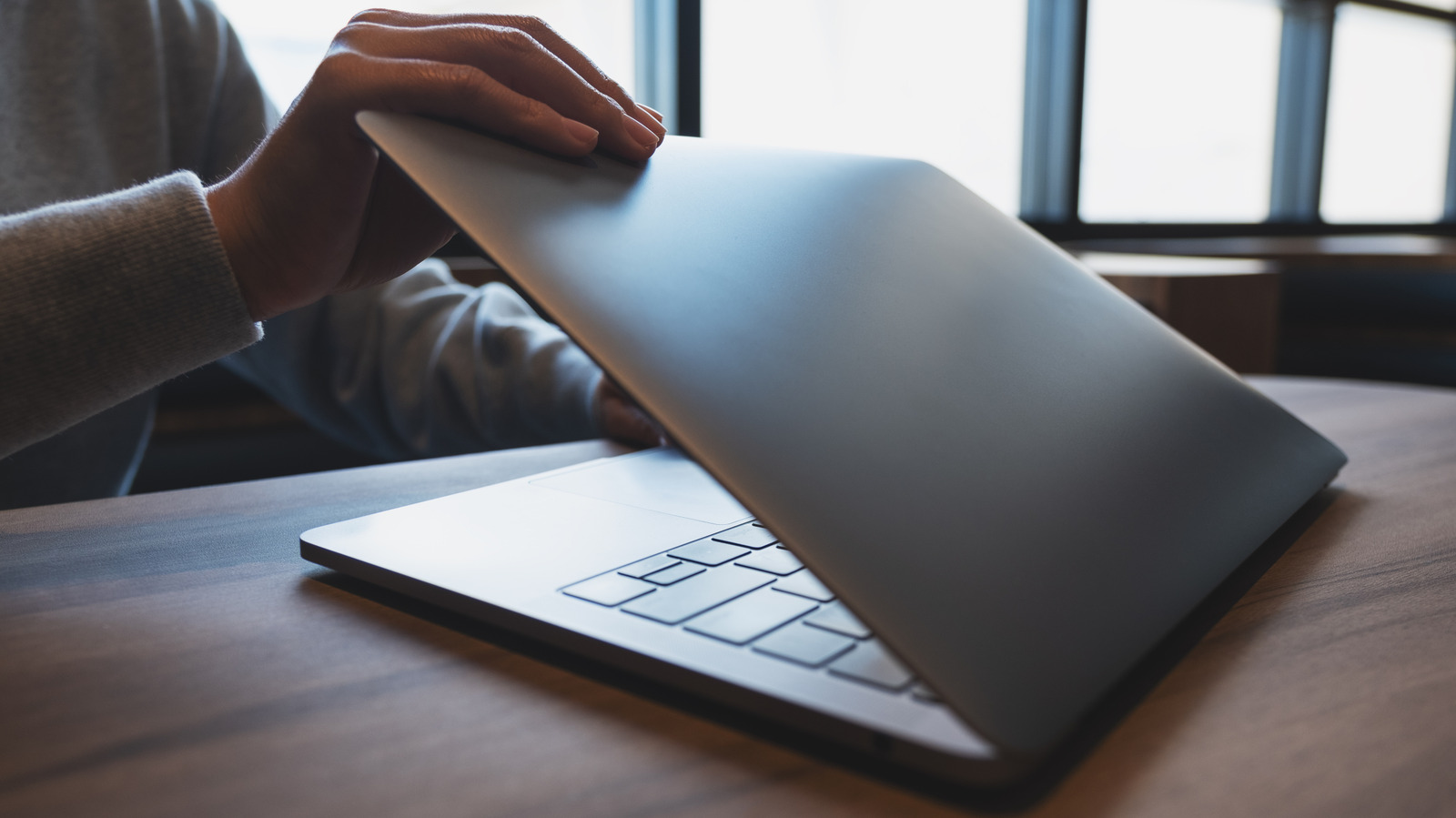 A person closes a laptop on a wooden table.