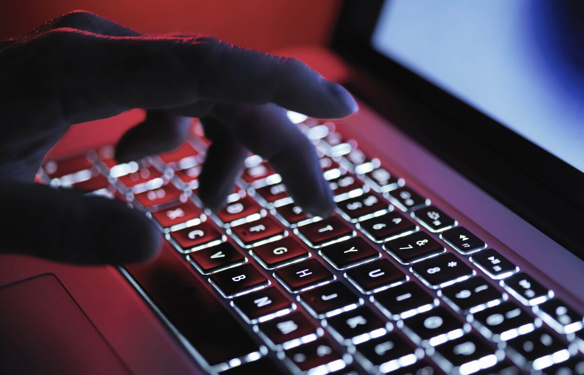A person's hand over a laptop keyboard in red and blue light.