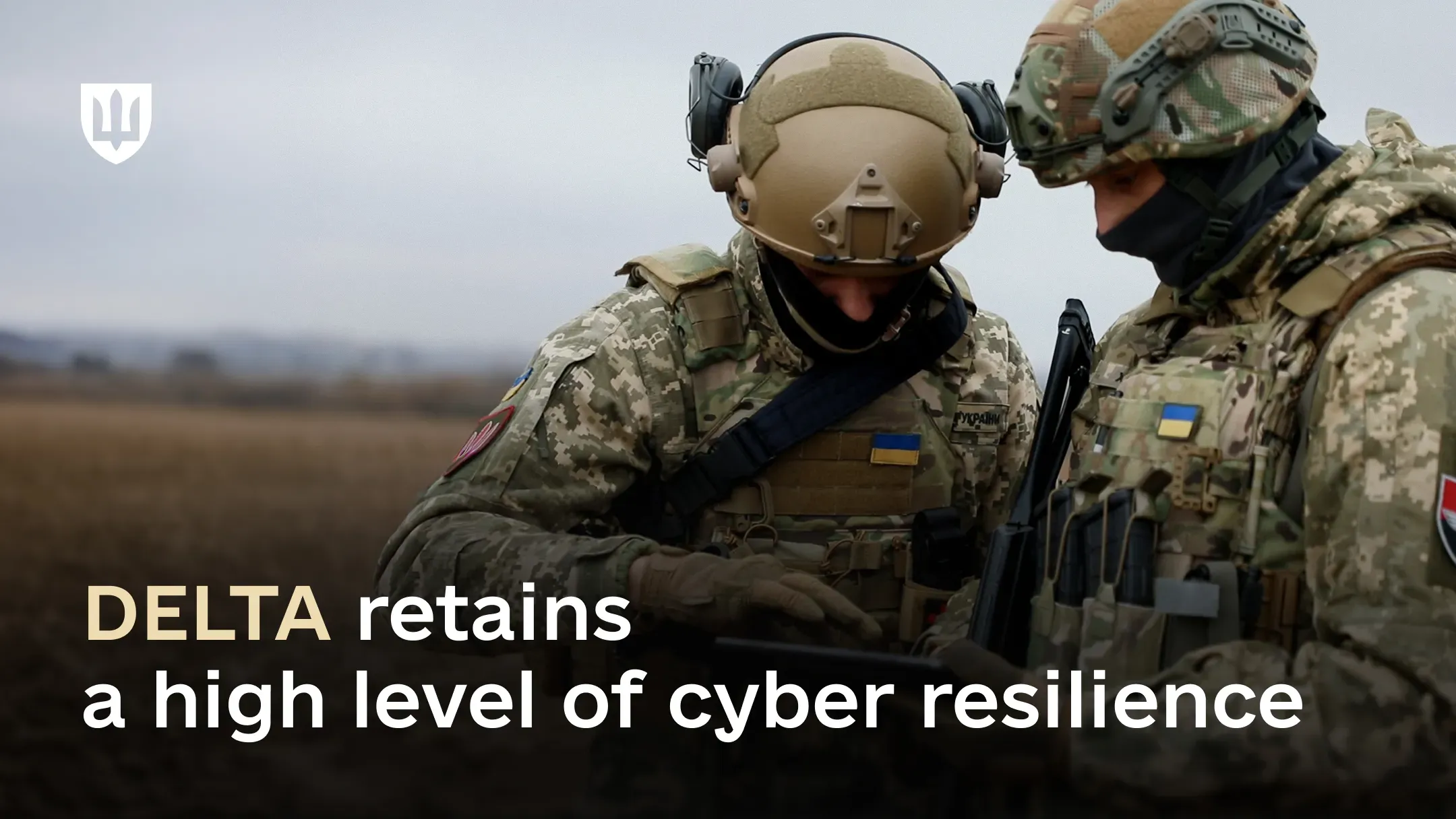Two Ukrainian service members in combat gear look at a tablet while standing in a field.