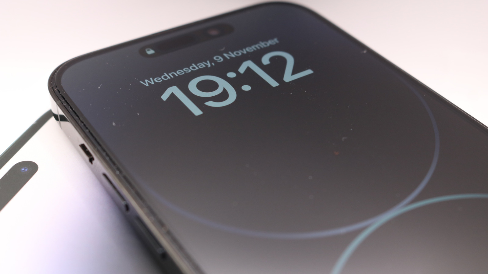 An iPhone displays a dimmed Always-On Lock Screen beside a person's hand.
