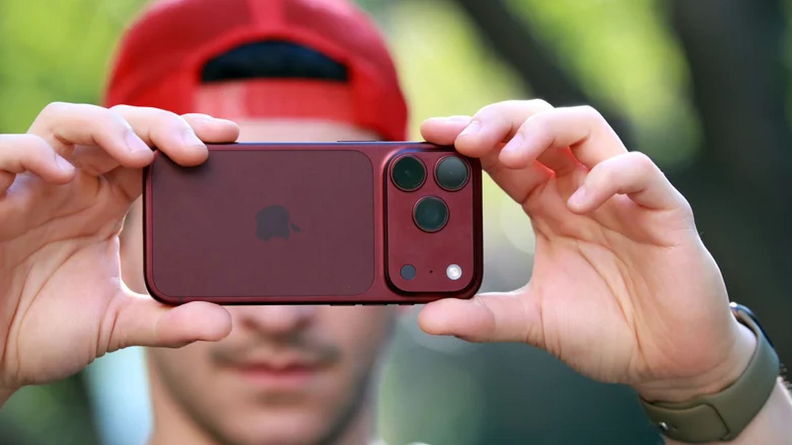 A reviewer holds a red iPhone horizontally to take a photo.
