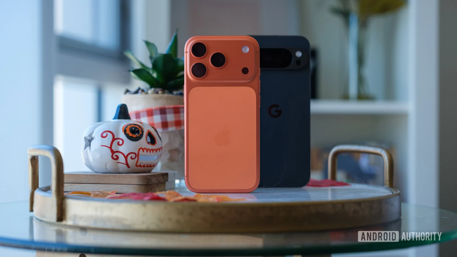 An orange iPhone stands in front of a dark Google Pixel phone on a tabletop.